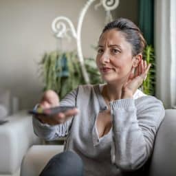 Woman adjusting her hearing aid while watching TV.