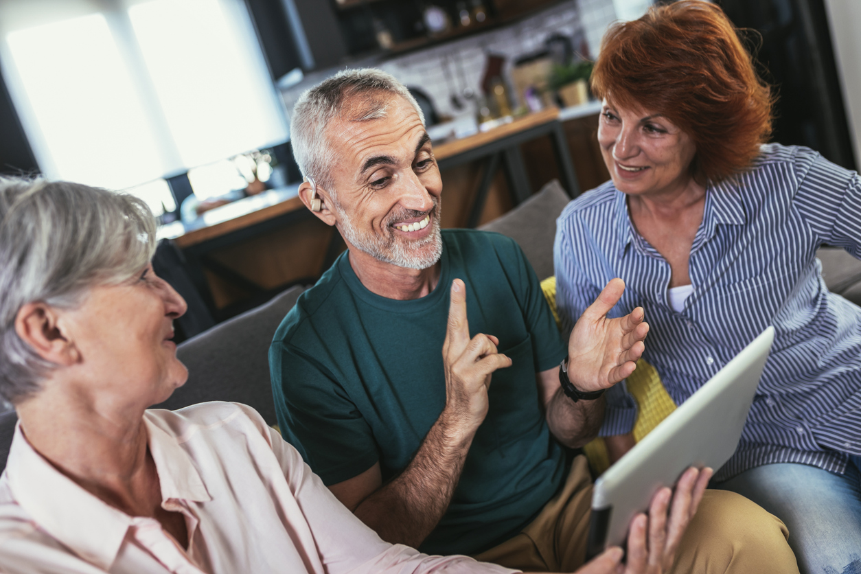 Man with a hearing aid looking at a tablet with his friends