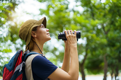 Smiling birdwatcher holding binoculars and wearing a wide-brimmed hat.