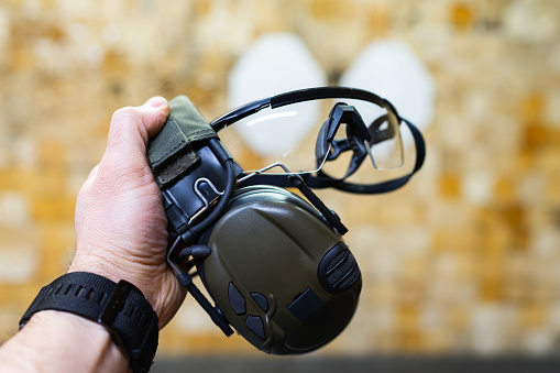 Close-up of active headphones and protective glasses in the hand of a person at a shooting range.