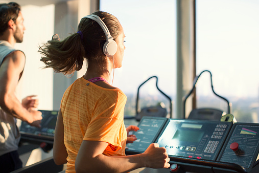 Group Of People Running on treadmill in a gym. Focus on a woman with headphones.