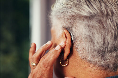 Senior woman touching the hearing aid in her right ear.